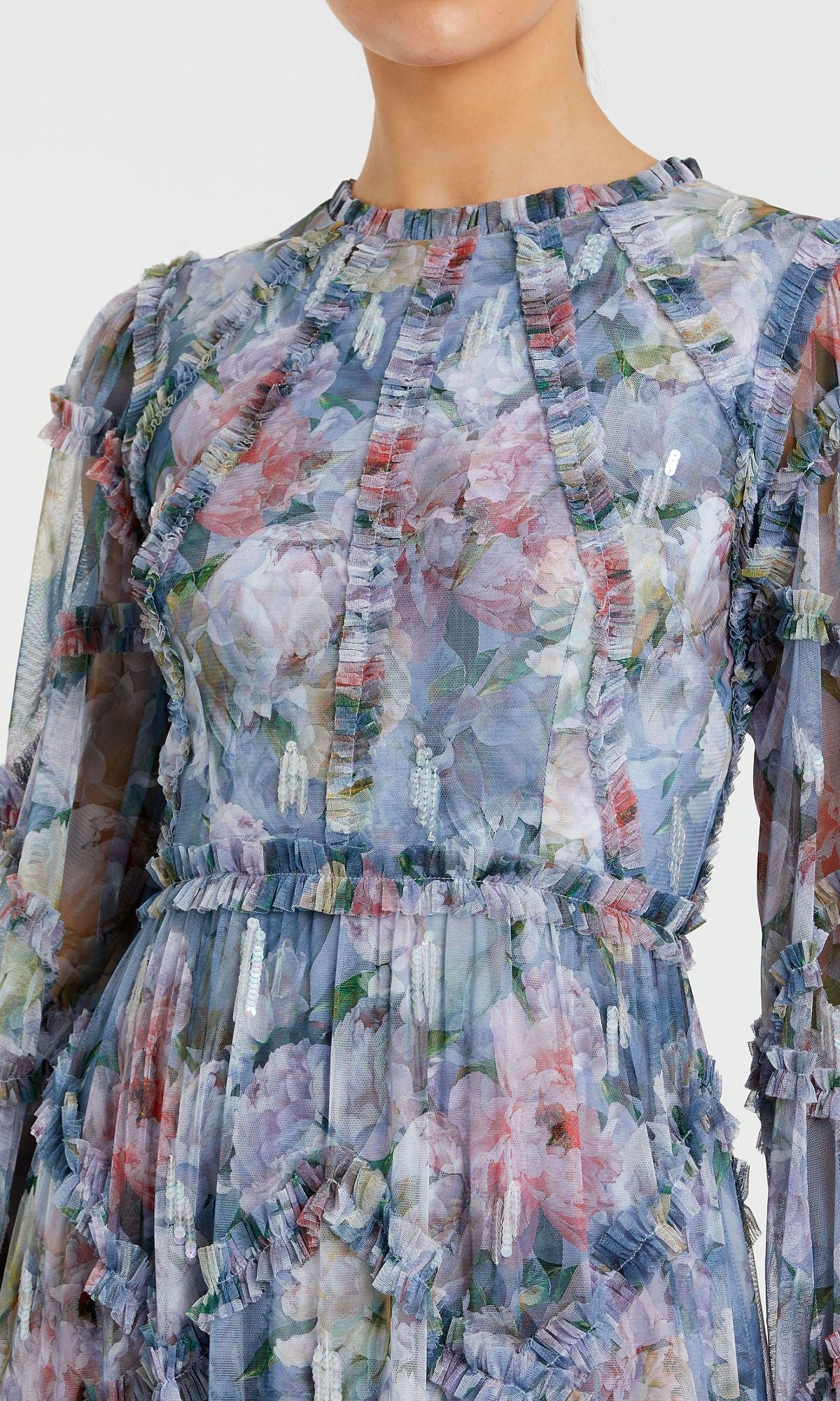 Close-up of a person wearing the Modest Long Print Formal Dress: Mac Duggal 8098, a sheer formal gown featuring floral prints and ruffle details in blue, pink, and green. The person's face is partially cropped from view.